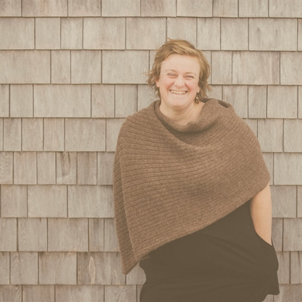 Jessie Harrold standing against a wall smiling warmly