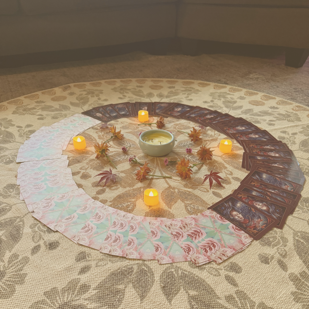 An altar in the centre of a circular rug with lit candles, oracle cards spread around it and leaves surrounding